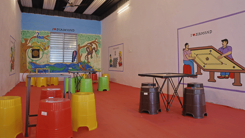 A wide view of a play area at the VITS Select Diamond Resort, Sasan Gir. The room has a red floor, colorful stools, and walls with cartoon-style murals of animals and people playing games.