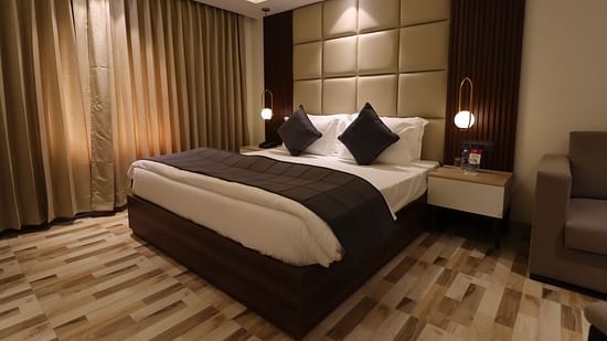 Side angle view of the studio view with a cozy view and a bed side table, partial view of the sofa at the corner - Mastiff Hotel, Dhanbad
