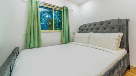 Bedroom with double bed, white bedsheet, green curtains, and wall-mounted lights at Nature Trails Durshet.