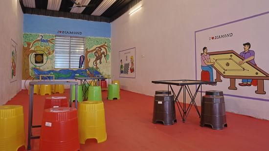 A wide view of a play area at the VITS Select Diamond Resort, Sasan Gir. The room has a red floor, colorful stools, and walls with cartoon-style murals of animals and people playing games.