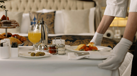 A staff member serving breakfast on a tray in a hotel room.