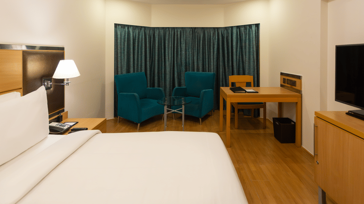 Superior Panoramic Rooms at The Residency Chennai featuring a plush bed with fresh linen facing the TV on a counter beside which is a work desk and a sitting space by the window