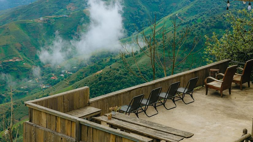 A scenic view of misty, green mountains from a balcony or terrace with outdoor furniture.