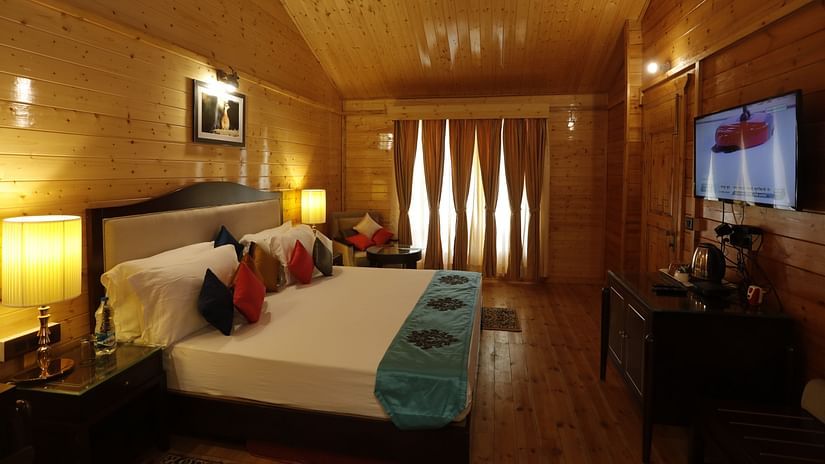 A well-appointed hotel room at Digantaa Resort in Mukteshwar featuring a spacious bed, wooden paneling, soft lighting, and a wall-mounted flat-screen television