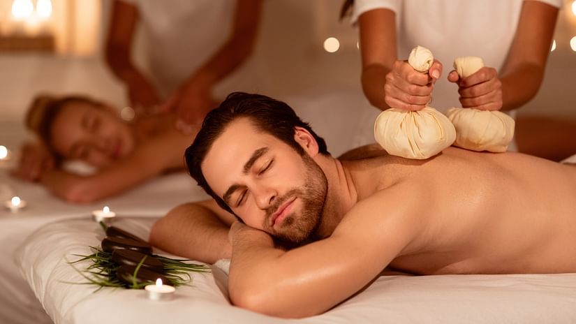 A couple undergoing massage, laying on white beds, assisted by two practitioners. 