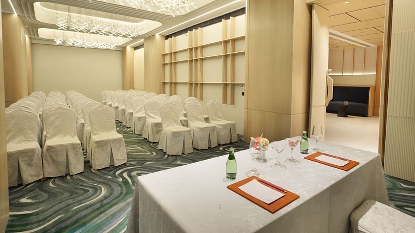 Angled view of a meeting room with white-covered chairs in rows and a white-draped table with red accents - The Orchid Hotel, Chandigarh
