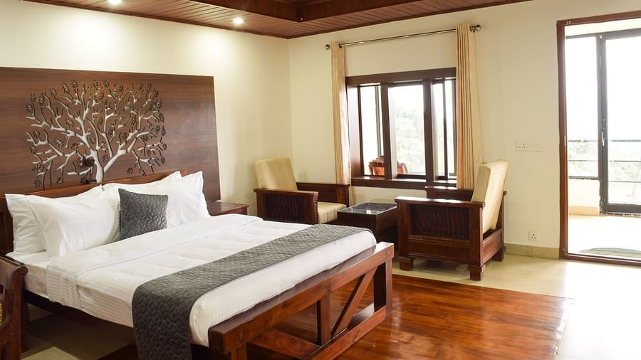 A side angle shot of the premium room featuring a king size bed, a seating area with two couches and a table  and a private balcony | A side angle shot of the suite at the resort feature a expansive balcony that overlooks the lush green valleys, king size 
