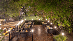 A dimly lit outdoor dining setting at night, with multiple tables illuminated by warm lights at The Golden Tusk, Jim Corbett