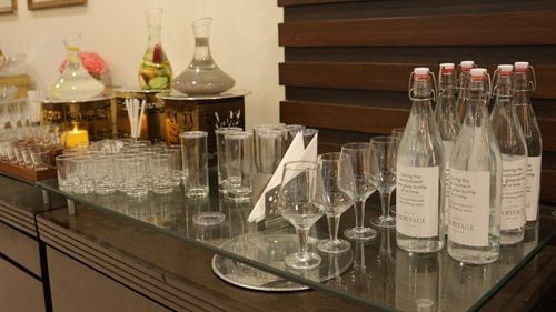 A glass table with glasses and bottles neatly arranged on top of it. - Heritage Village Resorts & Spa