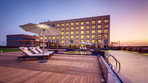 A hotel with a poolside area featuring lounge chairs, umbrellas, and a scenic sunset backdrop - Balaji Sarovar Premiere, Solapur