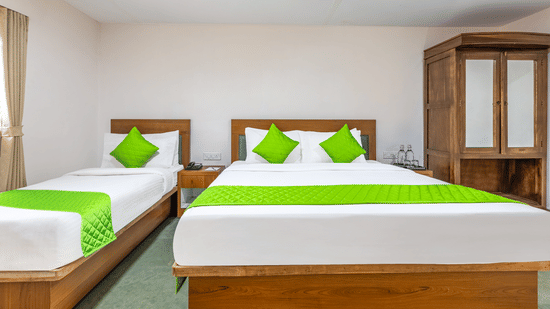 A Family Room at Nature Trails Durshet featuring two beds with green accent bedding wooden wardrobe stone tile flooring and white walls in a clean and simply furnished setting.