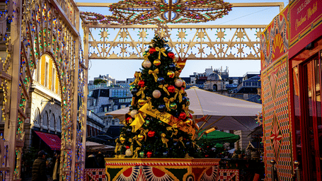 A decorated Christmas tree placed inside a highly ornate space with patterned textiles and an elaborate hanging light fixture.