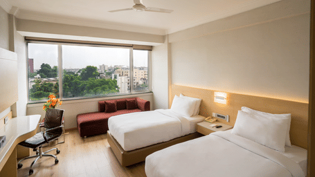 A Standard Room with twin beds, a large window, an office chair and a ceiling fan at Gemini Continental.