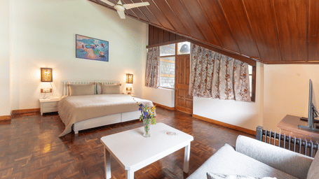 A spacious premium attic bedroom with polished wooden floors, white furniture, and a high timber-lined ceiling - Johnson Lodge & Spa, Manali