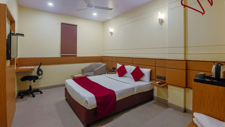 Bedroom with double bed, red runner, pillows, desk and wooden panel at Max Hotel Prayagraj.
