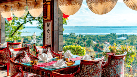 An indoor table set for guests at Ming Dynasty, located within Noor-Us-Sabah Palace, Bhopal, featuring large windows that provide a panoramic view of the lake.