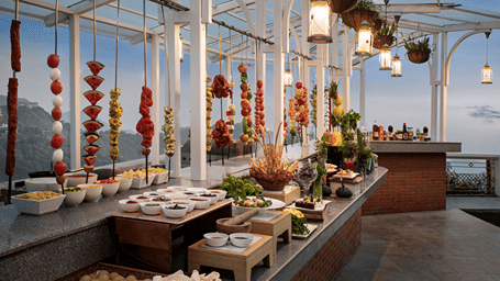 Food counters and colourful hanging decorations line a glass-roofed buffet area at Ramada by Wyndham Mussoorie Mall Road.
