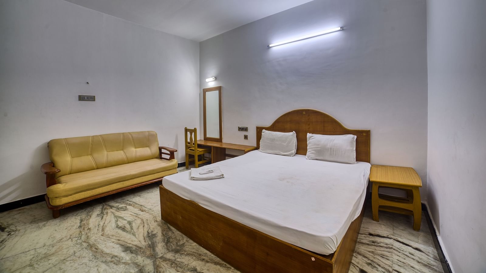 Comfortable double-bed room with sofa and ceiling fan in a minimal setup at Kailash Garden OMR.