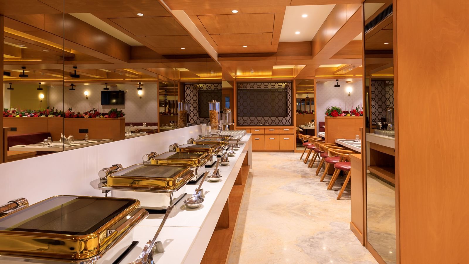 A brightly lit buffet area at Lords Eco Inn Apple Gate features multiple chafing dishes, ready to serve meals.