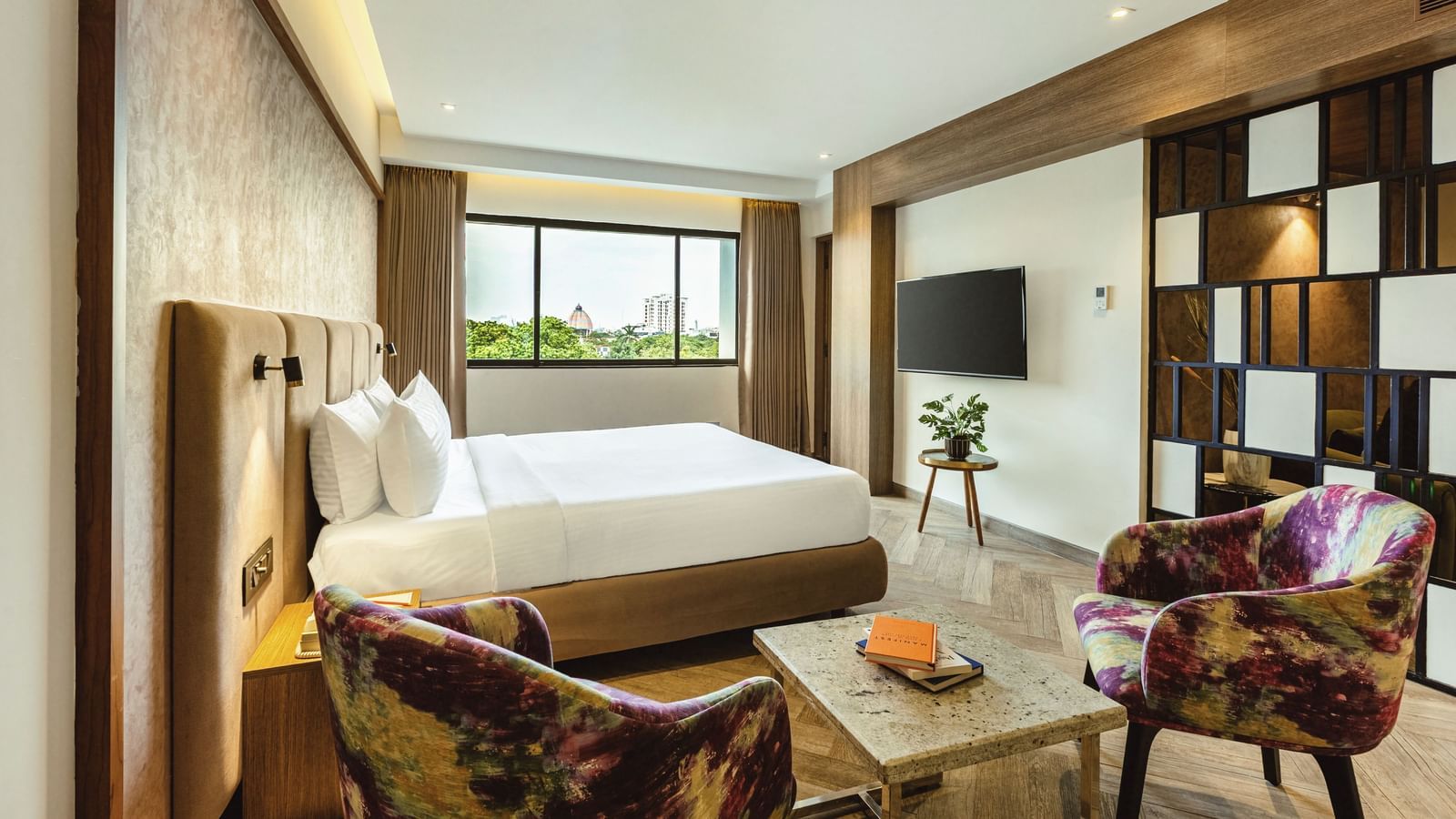 A wide-angle view of a room with a large bed and a seating area at Mango Hill Central, Chennai. A TV is on the far wall.