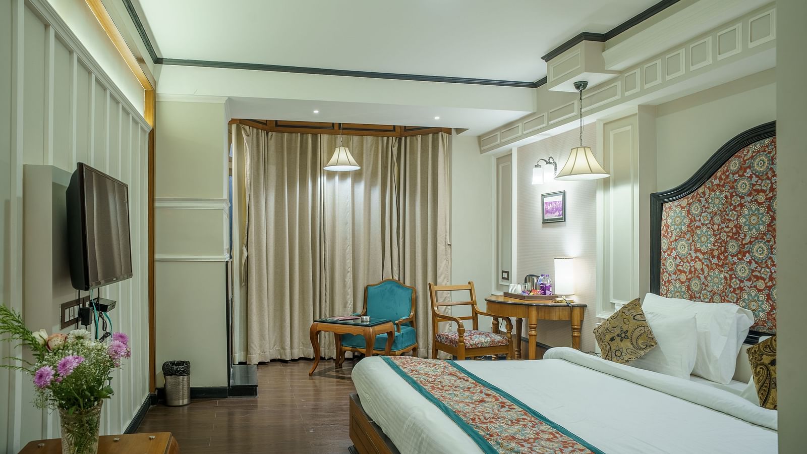A room at Orsino Spa Resort with a bed, a television, and a small sitting area, with large windows and light-coloured decor.