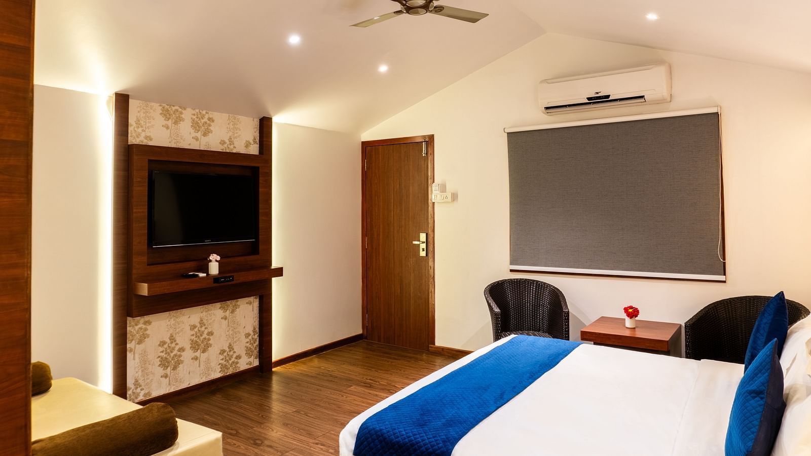 Lawn View Tent Room at The Grand Legacy Resort and Spa featuring wooden flooring, a wall-mounted TV, blue-accented bed, seating area, ceiling fan, and window blinds.