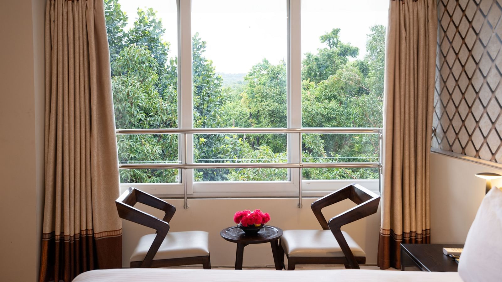 Image of two chairs and a small centre table by the window overlooking the lush green lawn | The Grand Legacy Resort and Spa