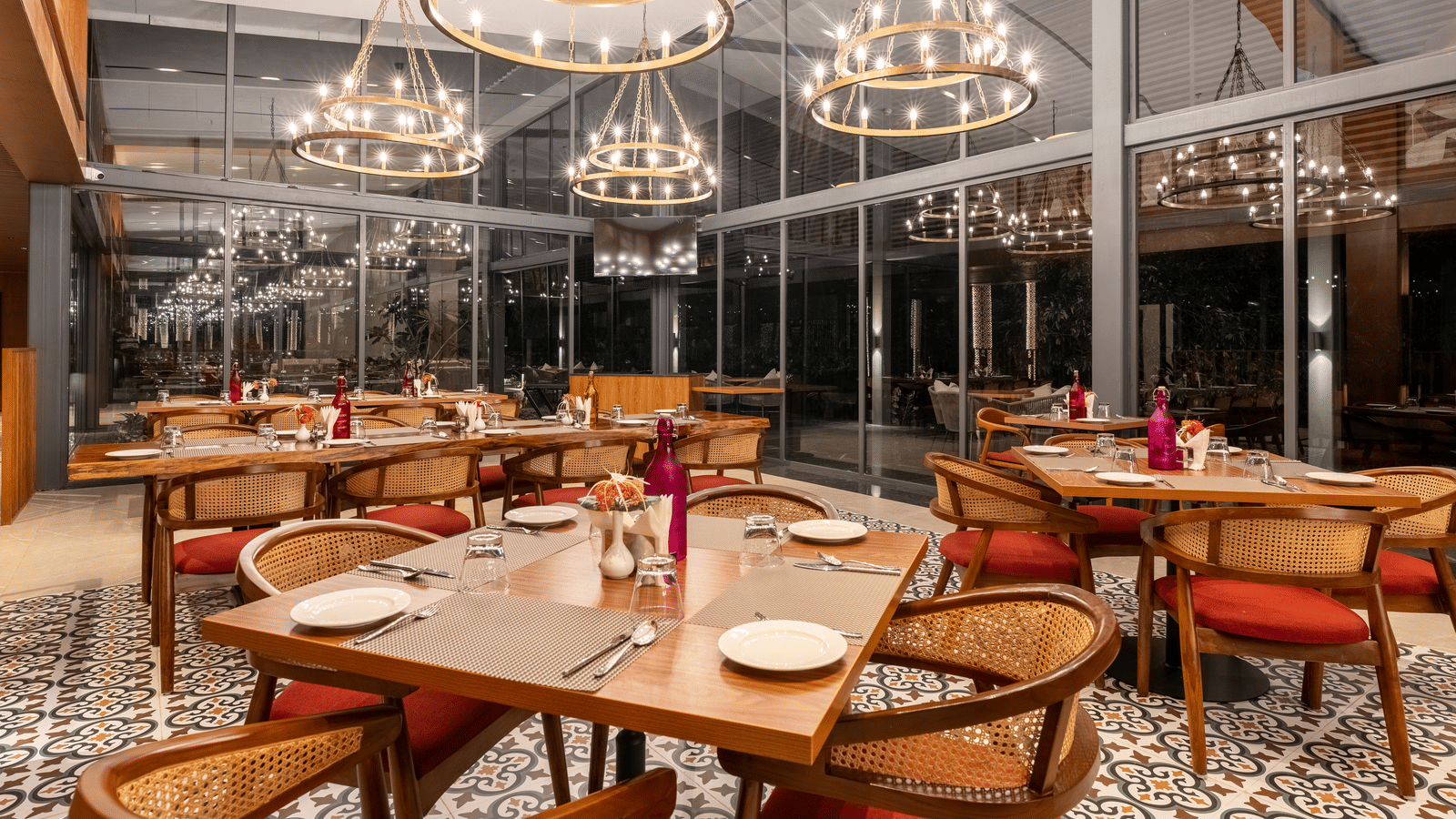 A  stylish restaurant setting at Wyndham Garden with round tables, modern lighting, glass facade interior, dark wood tables, and  circular chandeliers. 