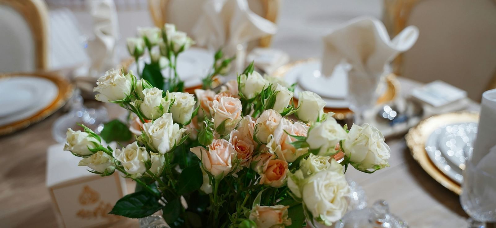 A close up shot of a beautiful flower vase with a lot of white and pink roses on a dining table.