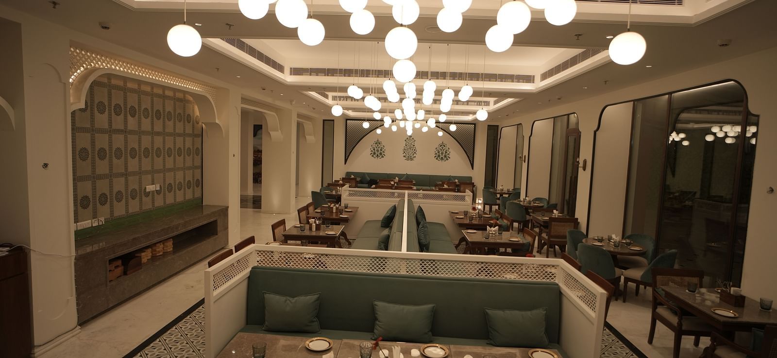 Full view shot of a restaurant with ample of warm lighting featuring well arranged dining tables along with cutlery Bhagirathi by RDB Atishay.
