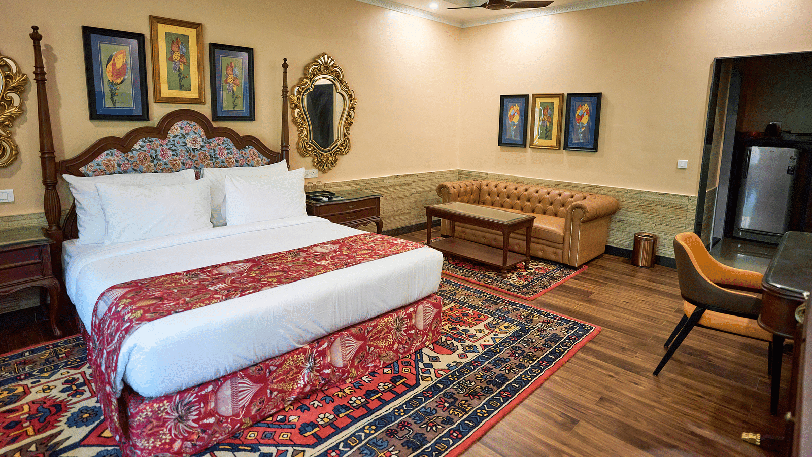 A spacious room with a large bed on one side and cushioned seating furniture on the other, adorned with wall-mounted frames for decoration at Mayfair Manor, Alibag