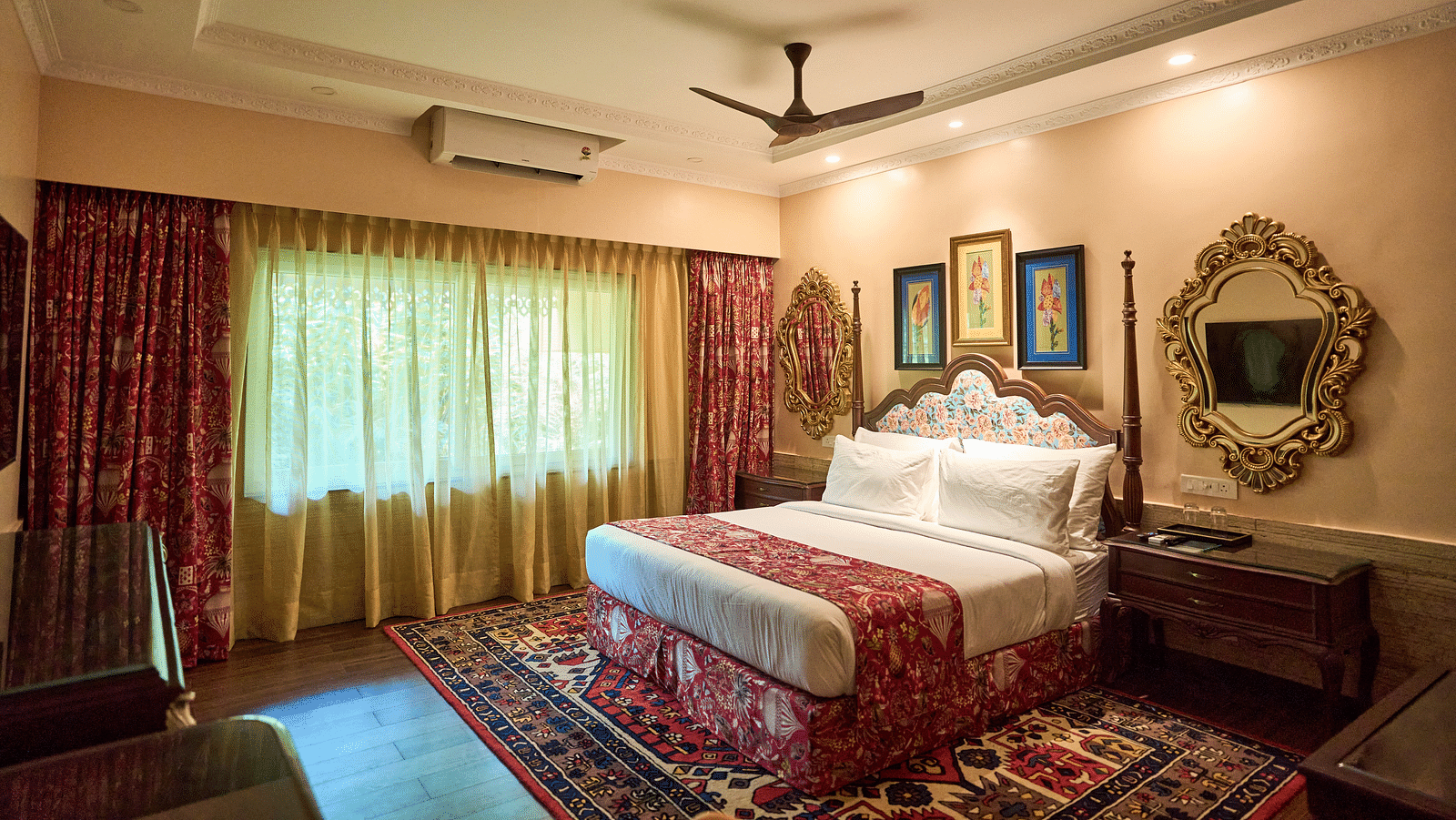 A spacious room featuring a large bed, wooden bedside tables, and windows draped with curtains at Mayfair Manor, Alibag