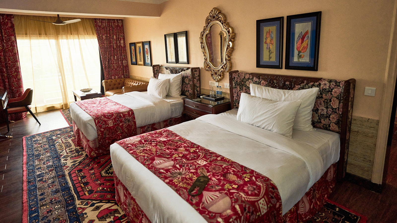 Side view of a spacious room featuring a double bed, wall-mounted frames for decoration, and windows elegantly covered with curtains at Mayfair Manor, Alibag