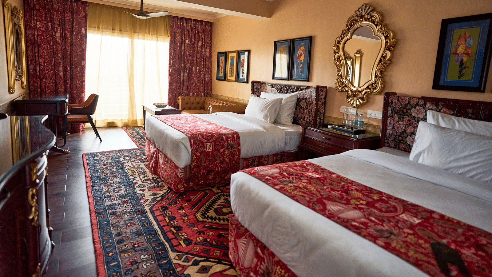 Side view of a spacious room featuring a double bed, wall-mounted frames for decoration, and windows elegantly covered with curtains at Mayfair Manor, Alibag