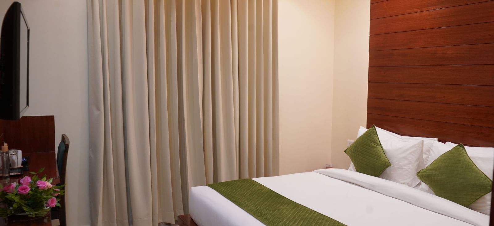 A clean hotel room with a bed, a bedside table, and curtains covering a large window.