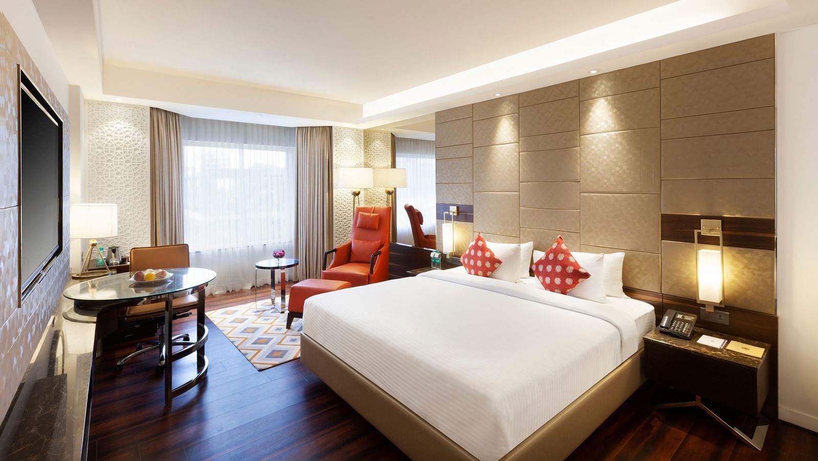 A spacious room with a large bed, wall-mounted TV, table, and cushioned chair, with curtains pulled to the side of the windows | Cenneys Gateway