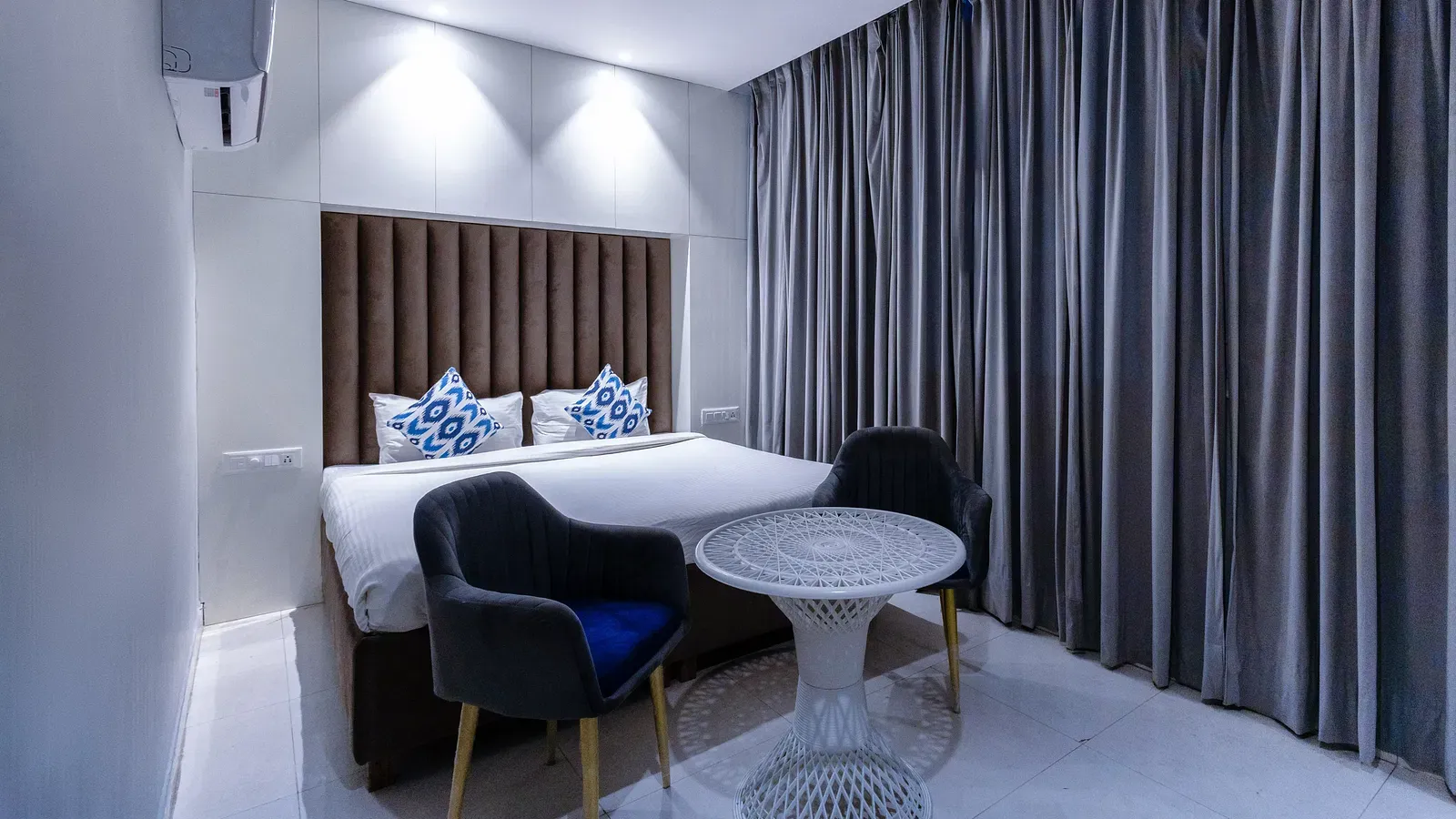 Deluxe Room featuring a king size bed with patterned cushions, two chairs, a table, and curtains. - Hotel Downtown17, Chandigarh