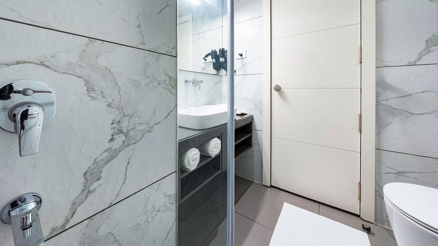A modern hotel bathroom with a white sink, toilet, and shower. The walls are tiled with a marble pattern -  Clarks Inn, Indore