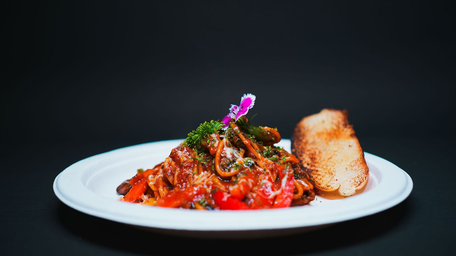 A gourmet pasta dish topped with rich tomato sauce, herbs, and an edible flower, served with a bread roll at D Café in Dip Holidays.