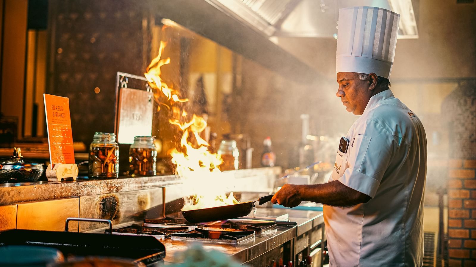 A chef expertly working at a live station, with flames rising from the pan, showcasing a vibrant culinary action