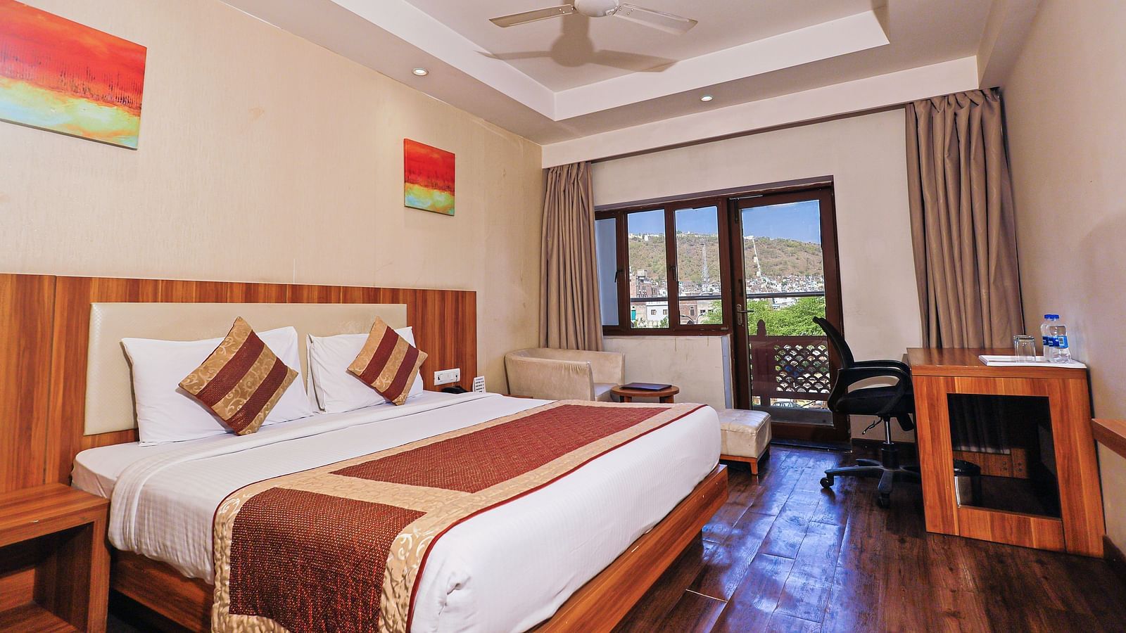 A low angle view of the bedroom with comfy bed and balcony, table and fan at Le Roi Udaipur