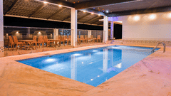 An outdoor swimming pool illuminated at night with several dining tables and chairs arranged on the surrounding deck at Abad Silvermist, Vagamon.