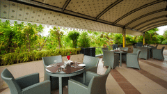 Open restaurant with roof on top featuring several sets of dining table and chairs at Arawali Ananta ELite, Ranakpur.
