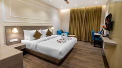 Premium Room at Pride Hotel Rishikesh featuring a plush bed decorated with towels and a TV in front of it mounted on the wall along with a sitting space arranged next to the window