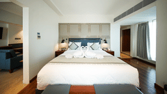 An interior view of a bedroom section within the Premium Suite Room at Pride Premier Udaipur. A double bed with pillows and a folded fabric arrangement sits in the centre of the room, positioned between bedside units.