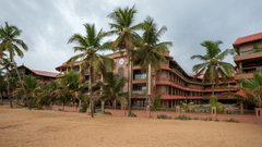 Uday Samudra Leisure Beach Hotel stands on a sandy shore lined with palm trees under a cloudy sky
