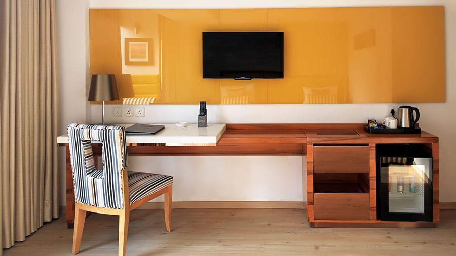 A wide angle view of  deluxe room at Barsana Boutique Hotel, Kolkata, with a work desk, chair, television, minibar, and kettle station.