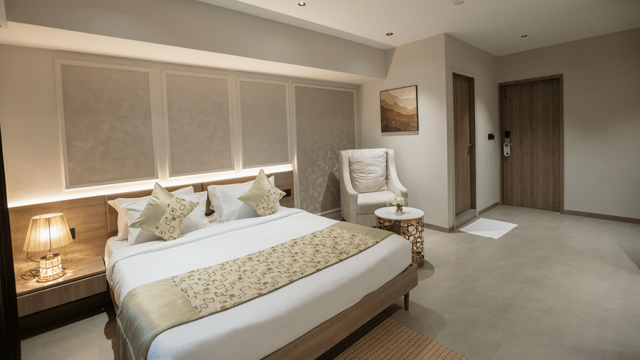 Elegant king guest room at Biznotel by Pride Surat featuring a large bed, ambient headboard lighting, and an armchair seating area.