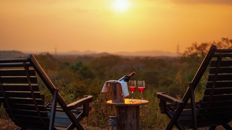 a close up shot of a table with glasses and bottles on it and chairs next to it and the sun setting in the background - Chunda Shikar Oudi, Udaipur