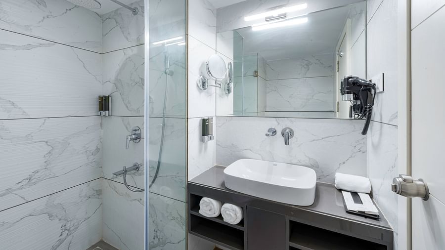 A modern hotel bathroom with a walk-in shower, a sink, a mirror, and a hairdryer - Clarks Inn, Indore